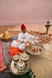 Image du Maroc Professionnelle de  Un marocain traditionnellement vêtu serve du thé à la menthe aux invités du grand Moussem de Tan Tan. Installée avec ses plateaux sur les hauteurs de la plage Chbika au environ de Tan Tan. Le Moussem est une sorte de foire annuelle, à la fois économique, culturelle et sociale. Il est classé par l'Unesco en 2005 comme patrimoine immatériel humain mondial. Chaque année la majorité des tribus et des grandes familles nomades du désert se retrouvent sur un site désertique pour célébrer ce grand Moussem où  danse, chants, course de chameaux et fantasia font partie des festivités. , Samedi 18 septembre 2004, ((Photo / Abdeljalil Bounhar)